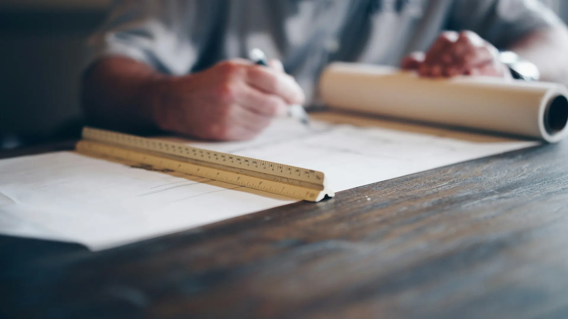 Hands drafting construction drawings with a scale ruler